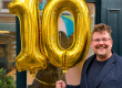 Kevin holding golden balloons in the shape of a 1 and 0