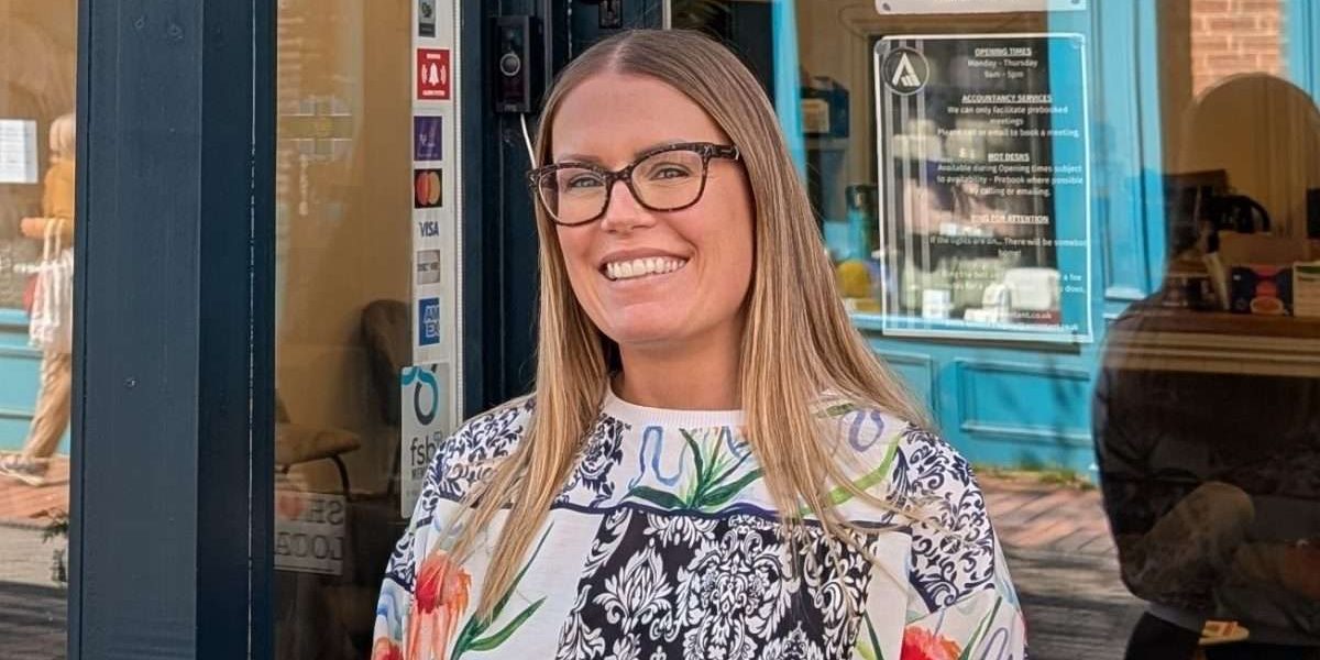 Gemma stood outside, smiling at the camera. She's wearing dark framed glassed and a patterned sweatshirt.