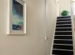A photo of the artwork hung on the left hand wall with the stairs leading the way up to the first floor in the background.