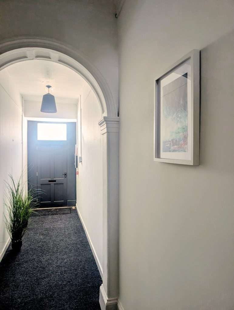 The artwork hanging on the right wall with the hall and front door to the left.