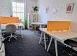 Our hot desk room - a bright room with dark grey carpet, white desks and bright yellow dividers.