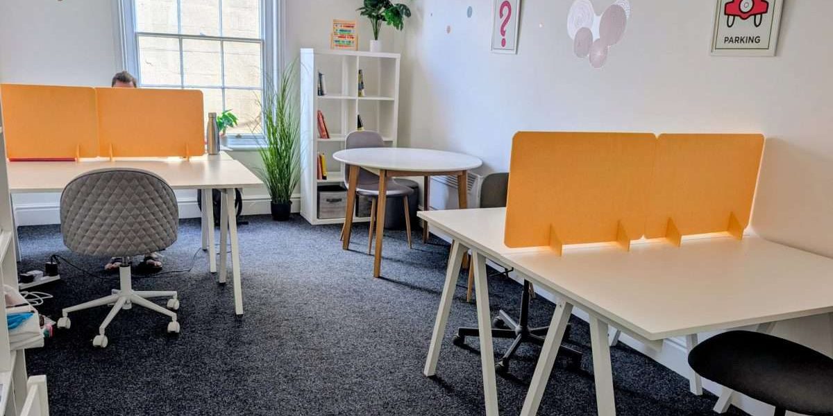 Our hot desk room - a bright room with dark grey carpet, white desks and bright yellow dividers.