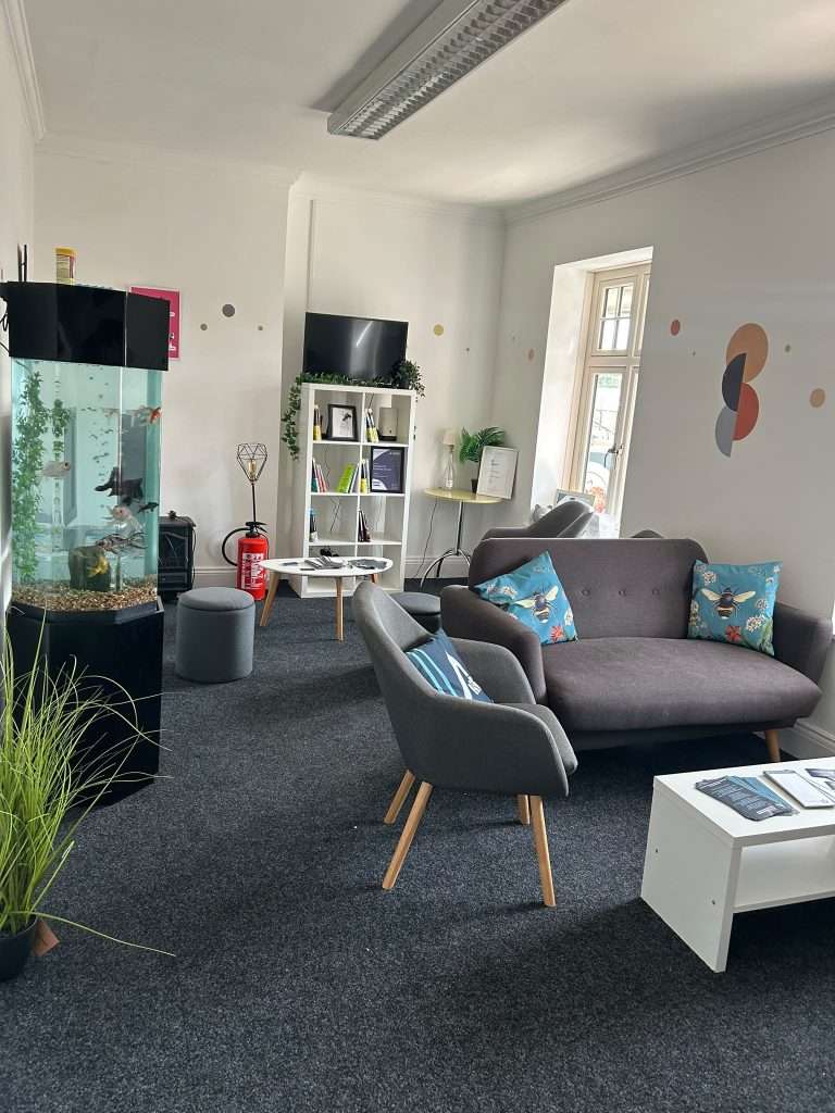 Our business lounge - a bright, airy room with white walls, grey sofas, a fish tank and dark grey carpet. 