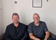 Photo of Kevin and Scott sat on the sofa in the Ascentant office. They're both smiling at the camera.
